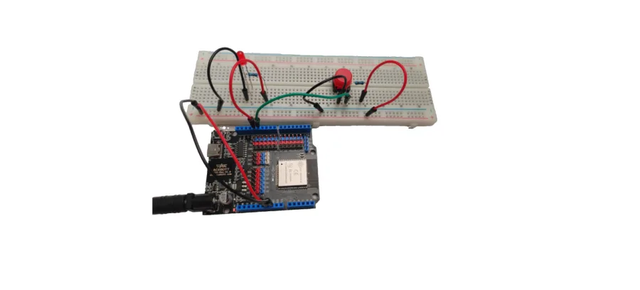 תצלום המעגל — לוח ESP32 מחובר ללוח ניסוי עם נורית אדומה ולחצן אדום