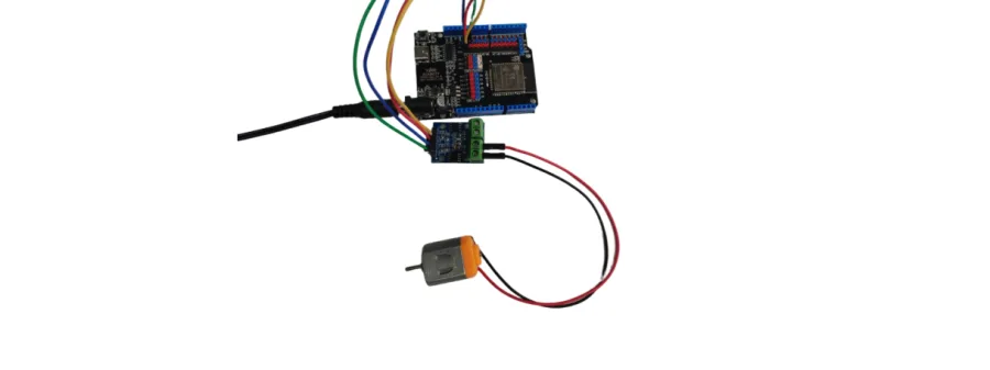 תצלום: לוח ESP32 מחובר בארבעה חוטים למודול נהג מנוע, שממנו יוצאים שני חוטים למנוע כתום